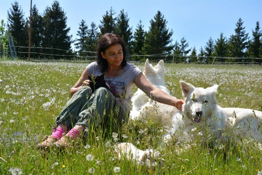 Leben in Einfachheit und in Verbindung mit Tieren und Natur. Marianne mit zwei Hunden, einem Kaninchen und einem Kater auf der Wiese sitzend