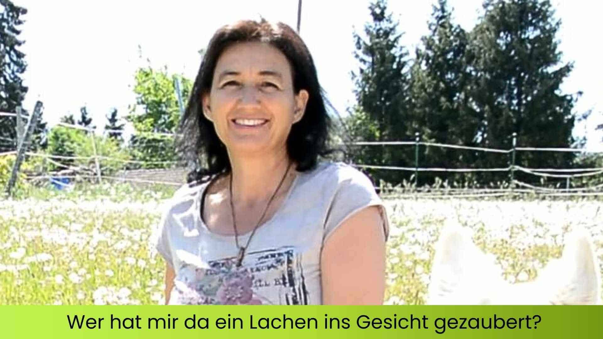 Marianne mit einem weißen Schäferhund in der Blumenwiese sitzend und lächelnd