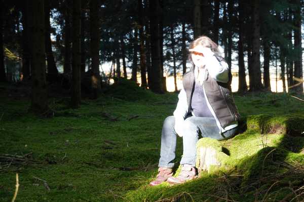 Marianne in einer Lichtung im Wald auf einem Baumstamm sitzend. 